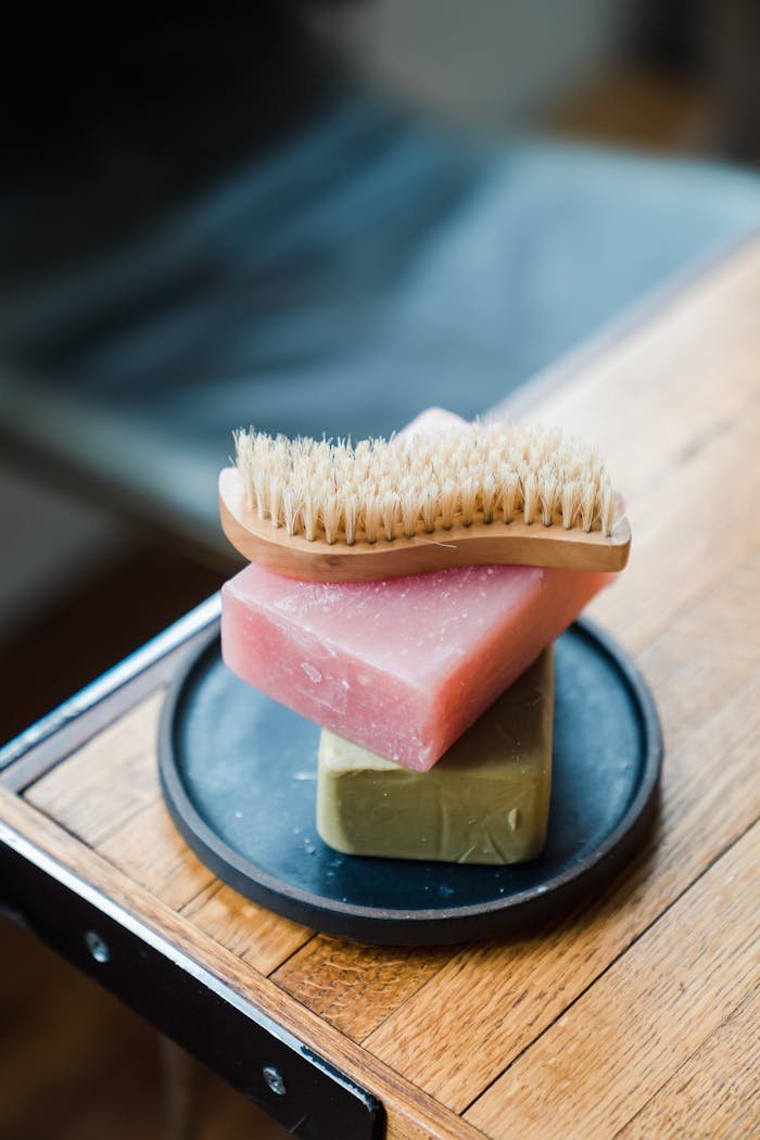 Stacked handmade soaps with a body brush on a wooden table, perfect for natural skincare routines.